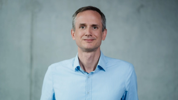 Professioneller Mann im blauen Hemd vor grauem Hintergrund, einladend und vertrauenswürdig.