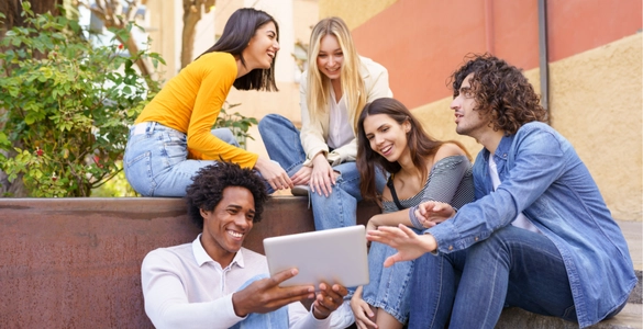 Junge Erwachsene genießen Teamarbeit im Freien mit Tablet, fröhliche Zusammenarbeit.