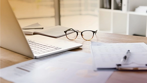 Moderner Arbeitsplatz mit Laptop, Brille und Dokumenten für produktives Arbeiten.