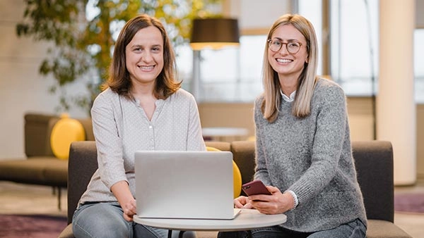 Moderne Büroatmosphäre: Zwei Frauen arbeiten lächelnd am Laptop.