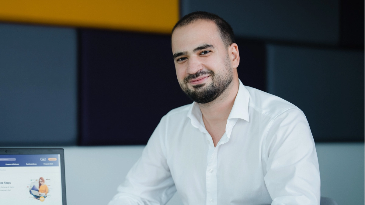 Professioneller Geschäftsmann im modernen Büro, lächelnd am Laptop.