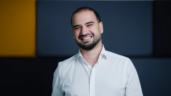 Lächelnder Mann in weißem Hemd vor modernem Hintergrund, professionell und einladend.