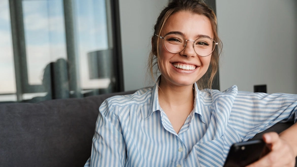 Lächelnde Frau mit Smartphone, modern und stilvoll, in entspannter Wohnatmosphäre.