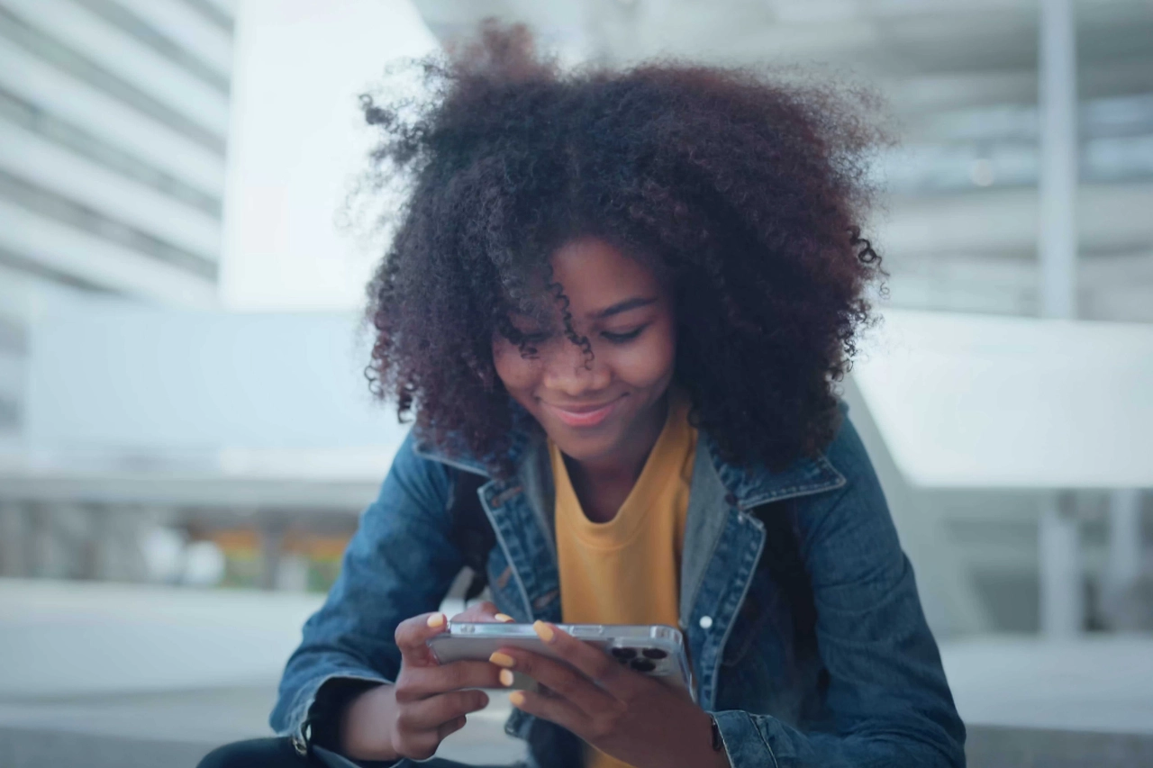 Junge Frau mit Smartphone, lächelnd, urbaner Hintergrund, moderne Kommunikation.
