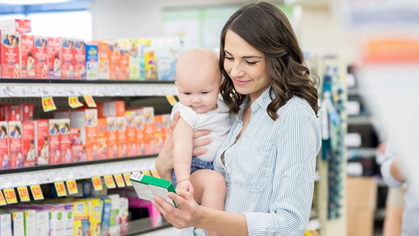 Mutter mit Baby beim Einkaufen von Babynahrung in einem Supermarkt.
