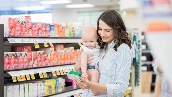 Mutter mit Baby beim Einkaufen in der Drogerie, lächelnd und Produkte betrachtend.