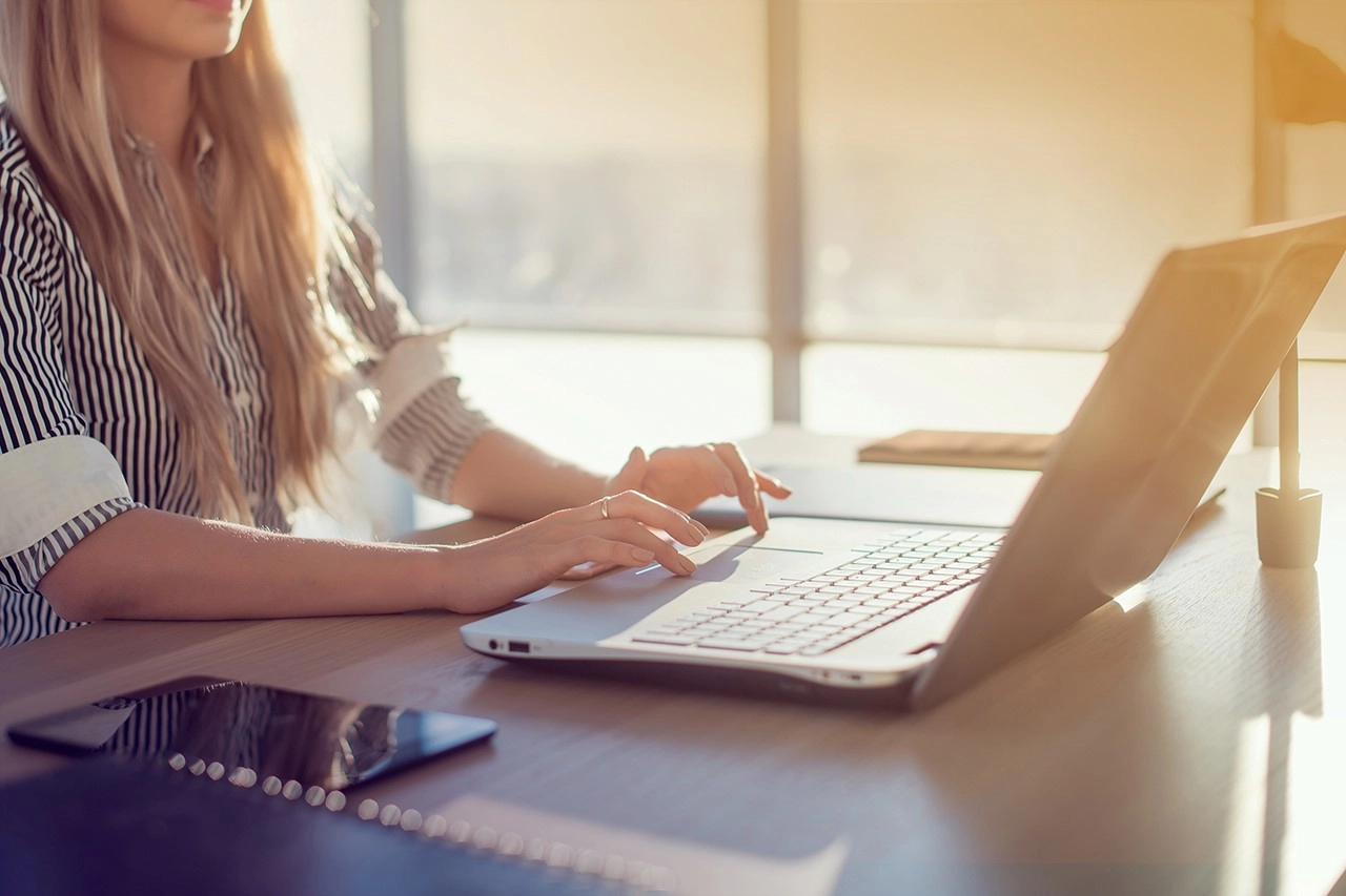 Moderne Büroarbeit: Frau am Laptop in sonnigem Büro, produktiv und fokussiert.