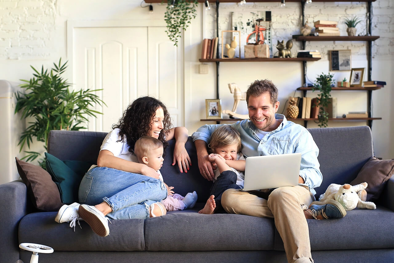 Glückliche Familie auf Sofa mit Laptop, modernes Wohnzimmer, harmonisches Zuhause.